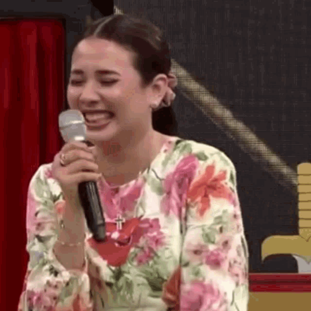 a woman in a floral dress is singing into a microphone and laughing .