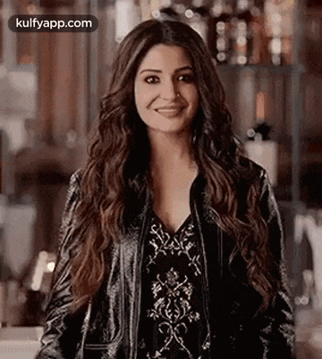 anushka sharma is wearing a black leather jacket and a black dress and smiling .