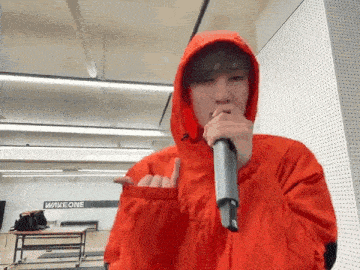 a man in a red hoodie is holding a microphone in his mouth .