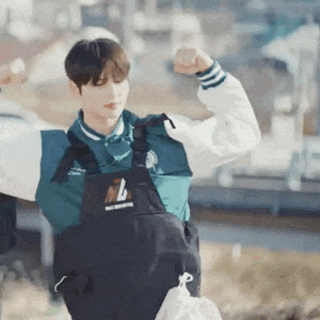 a young man wearing overalls is flexing his muscles while holding a bag .