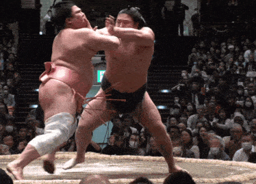 two sumo wrestlers are fighting in front of a crowd with a green exit sign