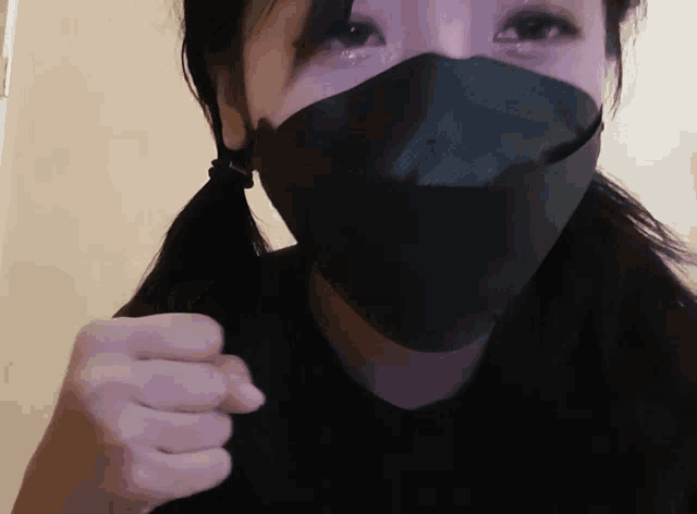 a woman wearing a black face mask holds her fist up in the air