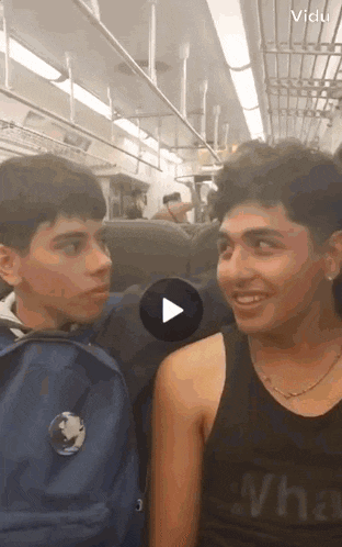 two young men are sitting next to each other on a train and one of them is wearing a black tank top with the word what on it