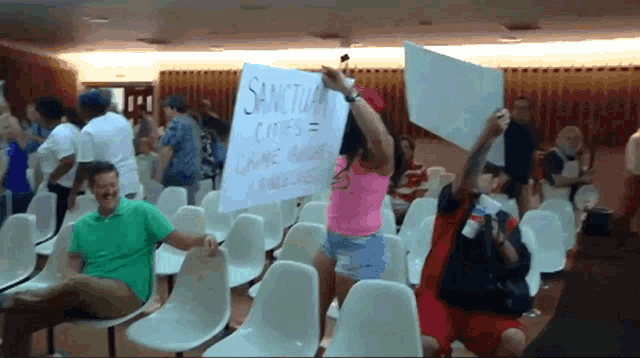 a woman in a pink shirt is holding a sign that says sanctuary comes