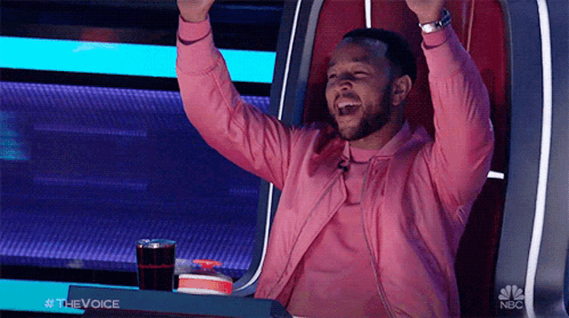 a man wearing a pink jacket is sitting in a chair with his arms in the air ..