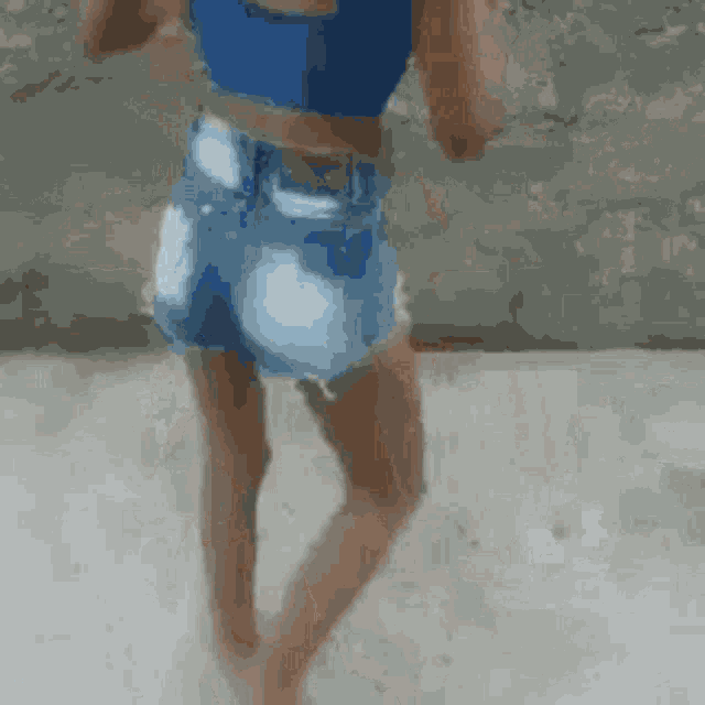 a woman in a blue crop top and denim shorts is walking on a sidewalk .
