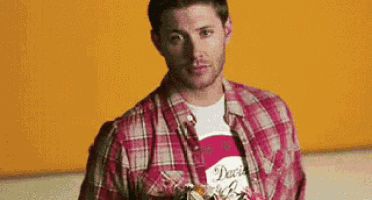 a man wearing a plaid shirt and a white t-shirt is standing in front of a yellow wall .
