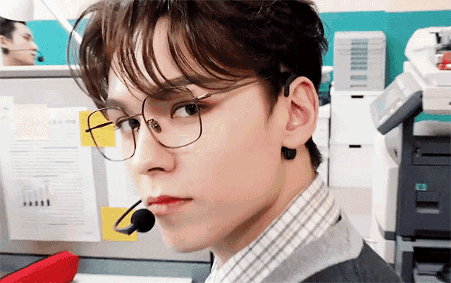 a young man wearing glasses and a microphone looks to the side