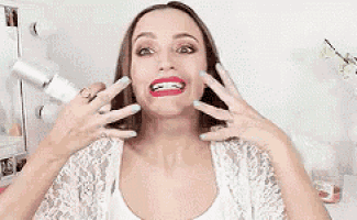 a woman with red lipstick and blue nails is making a funny face with her hands .