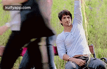 a man is sitting on a bench with his arm up in the air while a woman stands behind him .