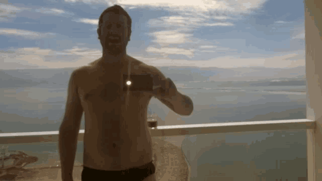 a shirtless man takes a picture of himself on a balcony overlooking a body of water