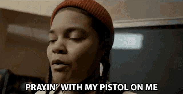 a woman wearing a beanie and braids is praying with her pistol on her chest .