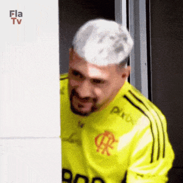 a man with white hair and a beard wearing a yellow shirt is standing in front of a door .