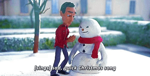 a man is standing next to a snowman wearing a red scarf and singing a christmas song .