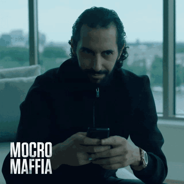 a man with a beard is looking at a cell phone with the words micro mafia on the bottom right