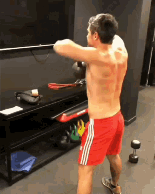 a shirtless man in red shorts is standing in front of a shelf with kettlebells on it