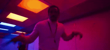 a man in a white turtleneck and lanyard is dancing in a dark room .