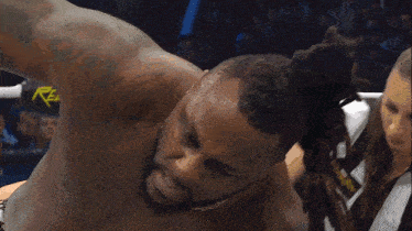 a man with dreadlocks is in a ring with a referee and a sign that says reb
