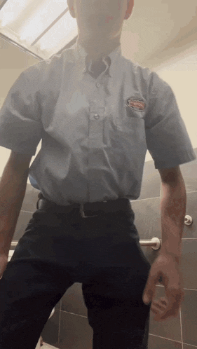 a man in a blue shirt and black pants stands in a public restroom