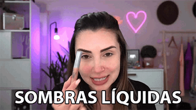 a woman is holding a brush in front of her face and the words sombras liquidas are on the bottom
