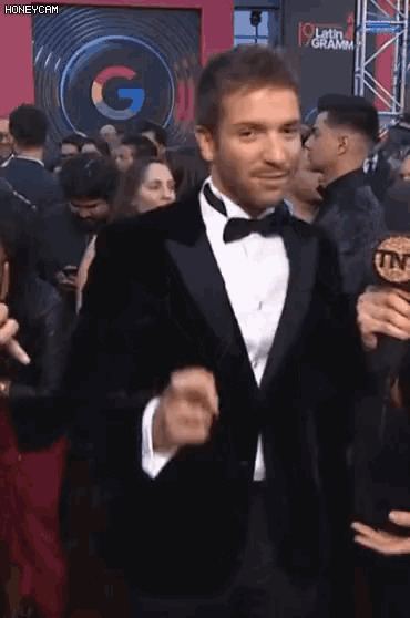 a man in a tuxedo is standing in front of a sign that says latin grammy