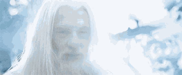 an older man with long white hair and a beard is standing in front of a tree .