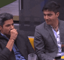two men in suits are sitting at a table and one is giving the middle finger