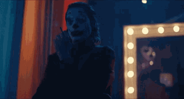 a man in a clown costume is smoking a cigarette in front of a mirror .