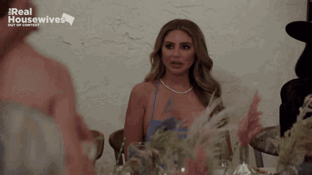 a woman in a blue dress sits at a table with real housewives out of context