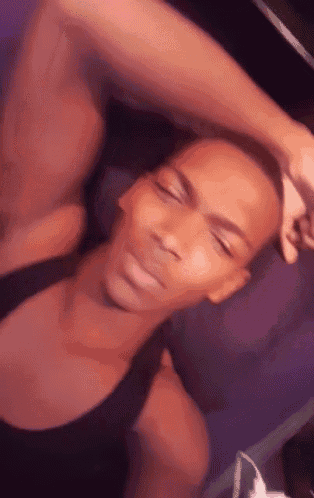 a man in a black tank top is laying down with his eyes closed and his hand on his head .