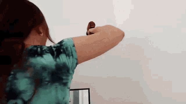 a woman in a tie dye shirt is standing in front of a white wall holding a red object .
