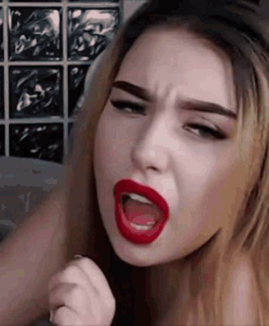 the woman is wearing red lipstick and making a funny face .