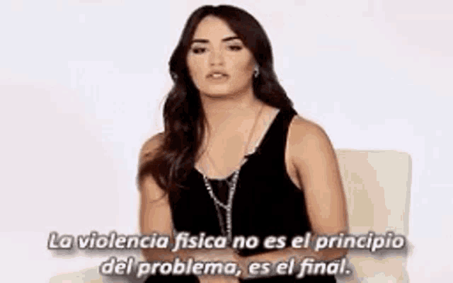 a woman in a black tank top is sitting in a chair with a quote in spanish .