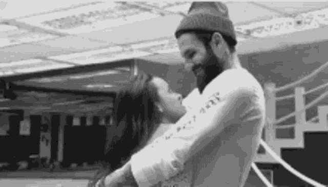 a man with a beard is holding a woman in his arms and kissing her .