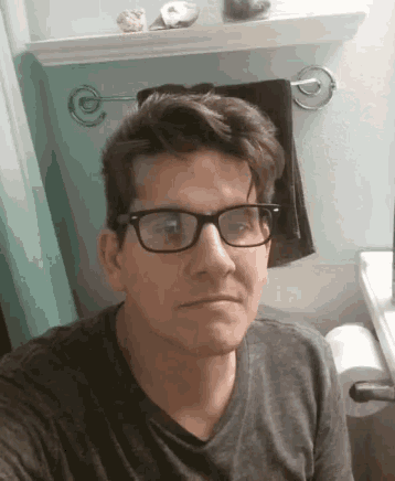 a man with glasses is taking a selfie in a bathroom