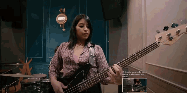 a woman is playing a bass guitar in a room with a sign that says " a " on it