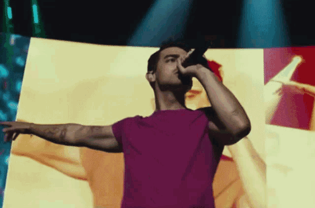 a man in a pink shirt is singing into a microphone on stage