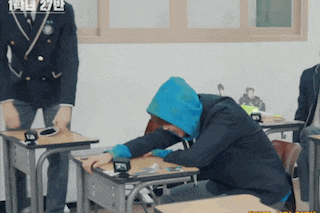 a man wearing a blue hoodie is sitting at a desk in a classroom