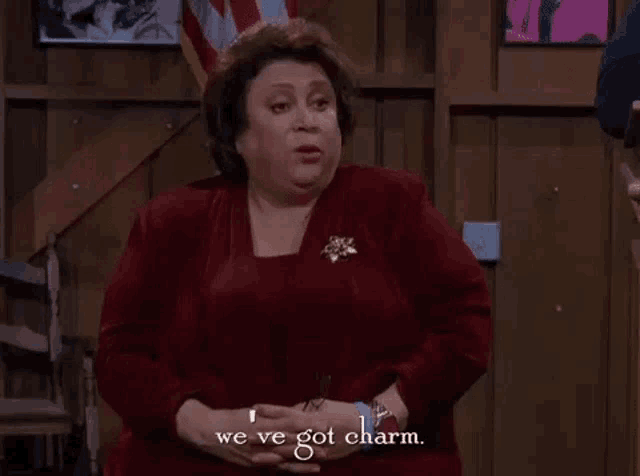 a woman in a red dress is sitting in a chair and saying `` we 've got charm '' .
