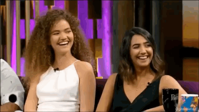 two women are sitting next to each other on a couch laughing
