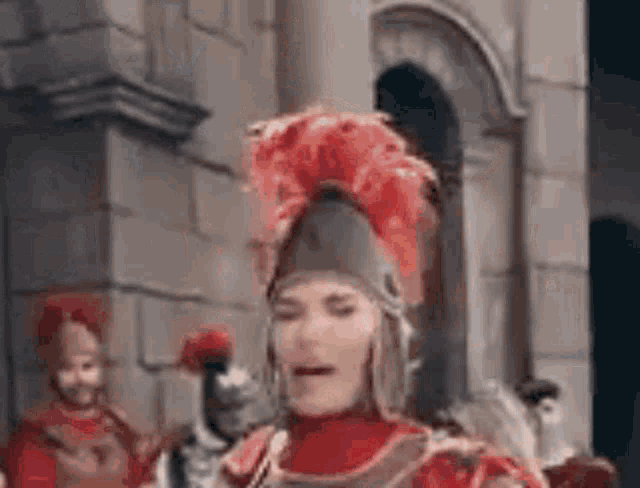 a man dressed as a roman soldier with a red feathered helmet is standing in front of a building .