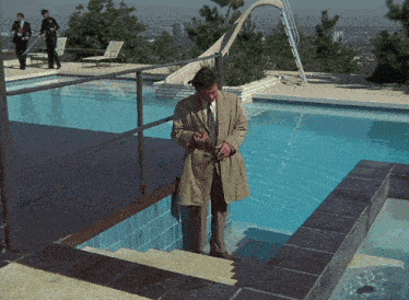 a man in a trench coat stands next to a pool