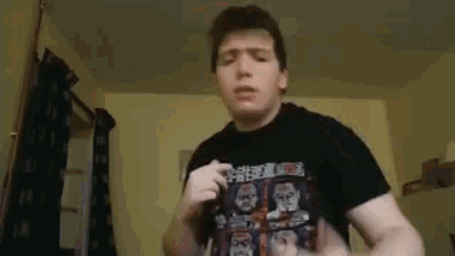 a young man wearing a black t-shirt with a picture of a man on it is standing in a room .