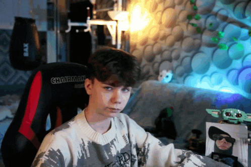 a boy wearing a chairman sweater sits in a room