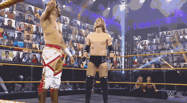 two wrestlers are standing in a wrestling ring with the w logo on the wall