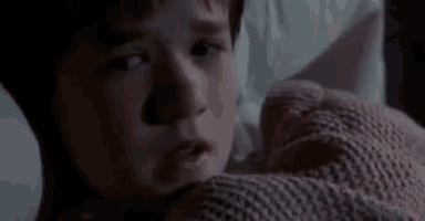 a young boy is laying in bed covered in a pink blanket and looking at the camera .