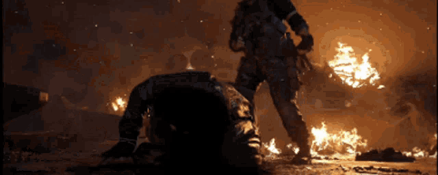 a man is laying on the ground in front of a fire while another man stands behind him