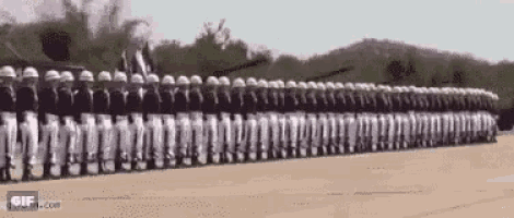 a row of soldiers marching in a parade in a field .