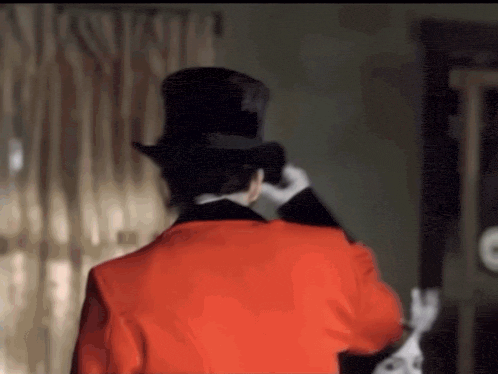 a man in a top hat and a red jacket is standing in a room .