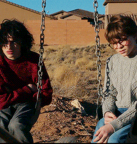 two young boys are sitting on a swing set